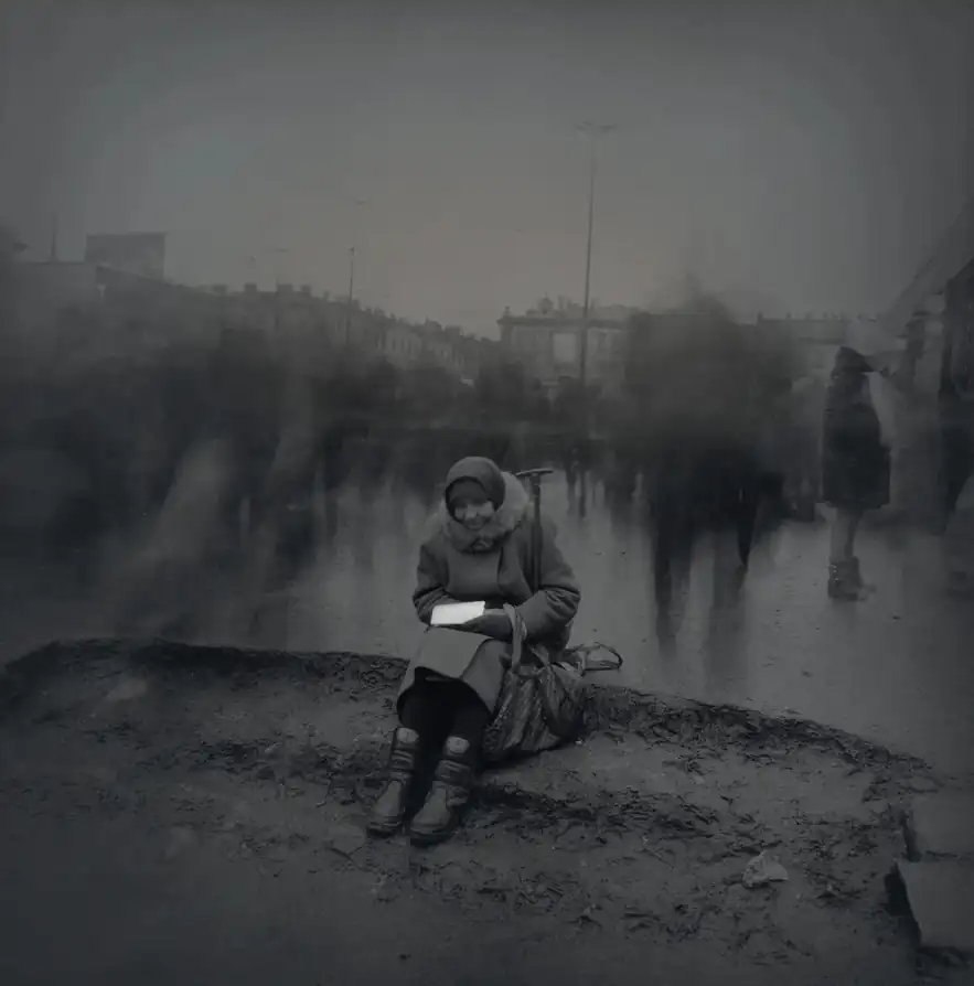 An elderly woman sits on muddy Haymarket Square as long-exposure pedestrians blur past behind her.