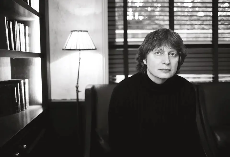 A black-and-white portrait of Alexey Titarenko seated beside bookshelves and a lamp.