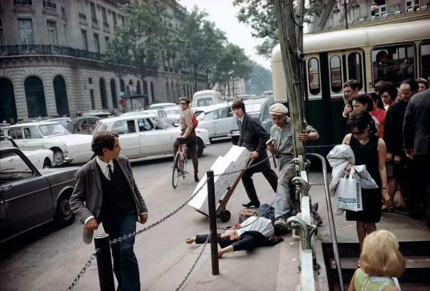 A man lies on the pavement beside a Paris Metro entrance as pedestrians pass.