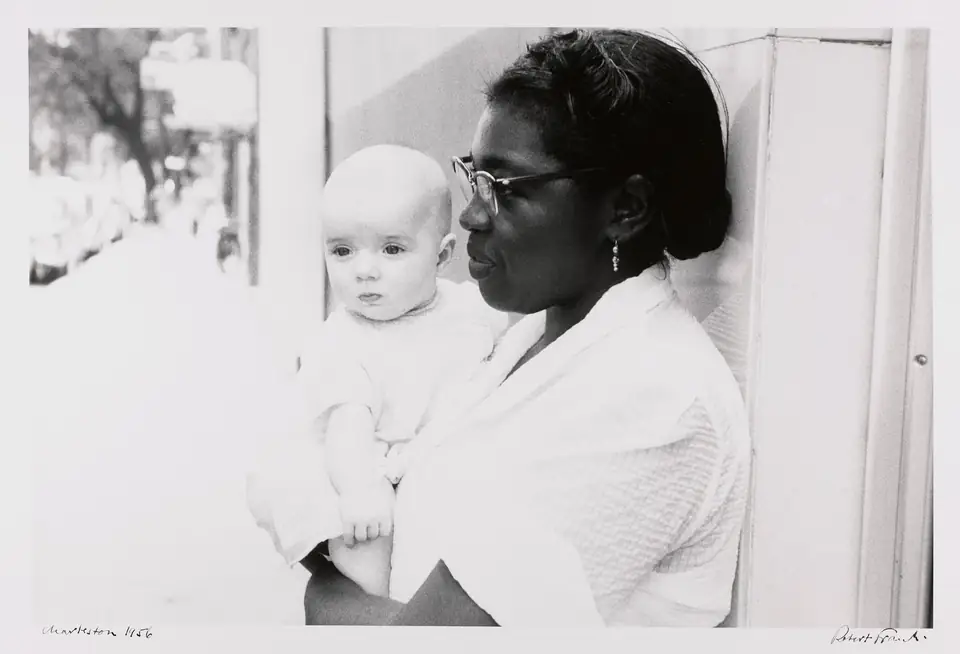 A woman wearing glasses holds a baby outside a building in Charleston.