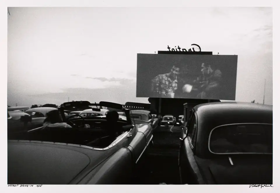 Rows of parked cars face a distant outdoor cinema screen in Detroit.