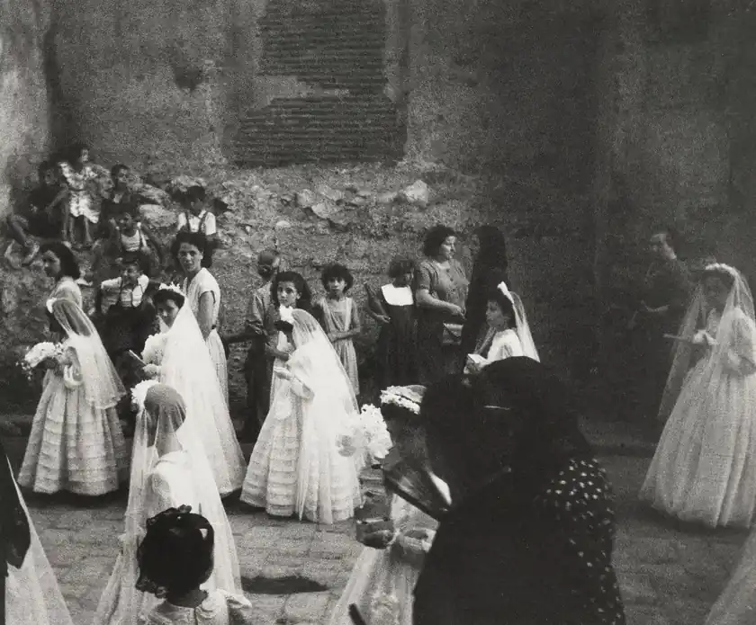 Women and girls in dresses gather in a stone courtyard.