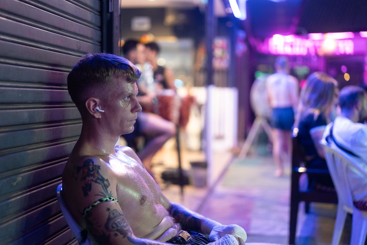 Frederik Trovatten sits shirtless beside a shutter, oiled up and waiting for his Muay Thai fight in Chiang Mai.