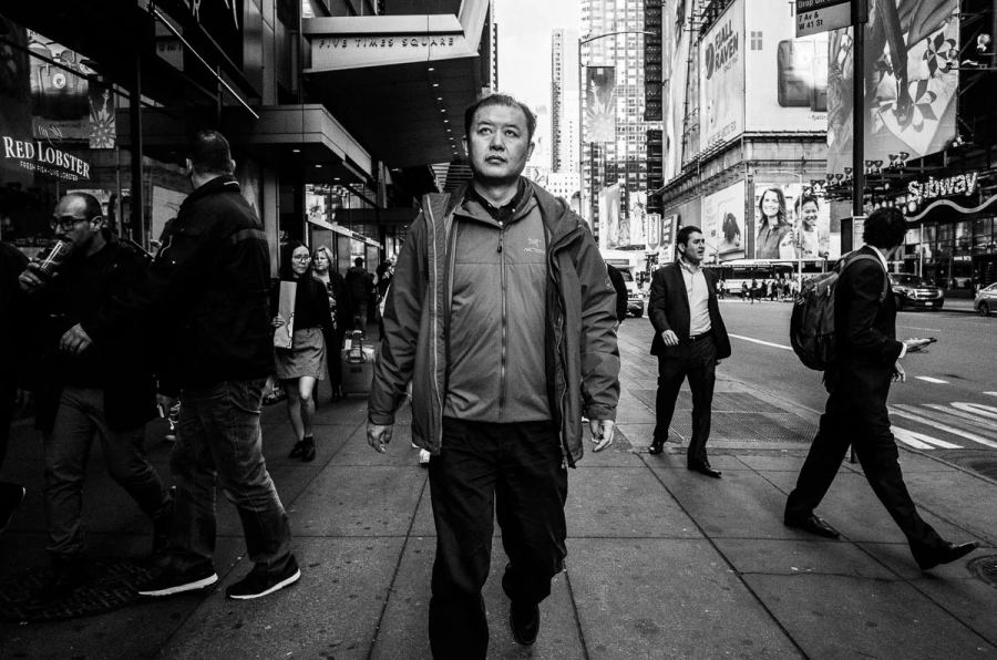 Black-and-white NYC street photograph of a man walking through Times Square