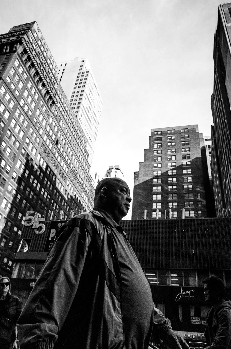 Black-and-white New York street photograph of a man beneath Midtown skyscrapers