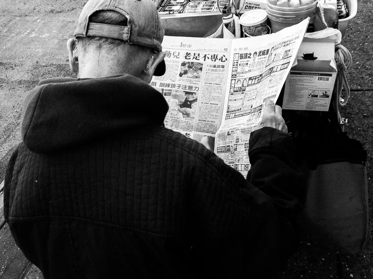 New York City street photography of a man reading a Chinese-language newspaper