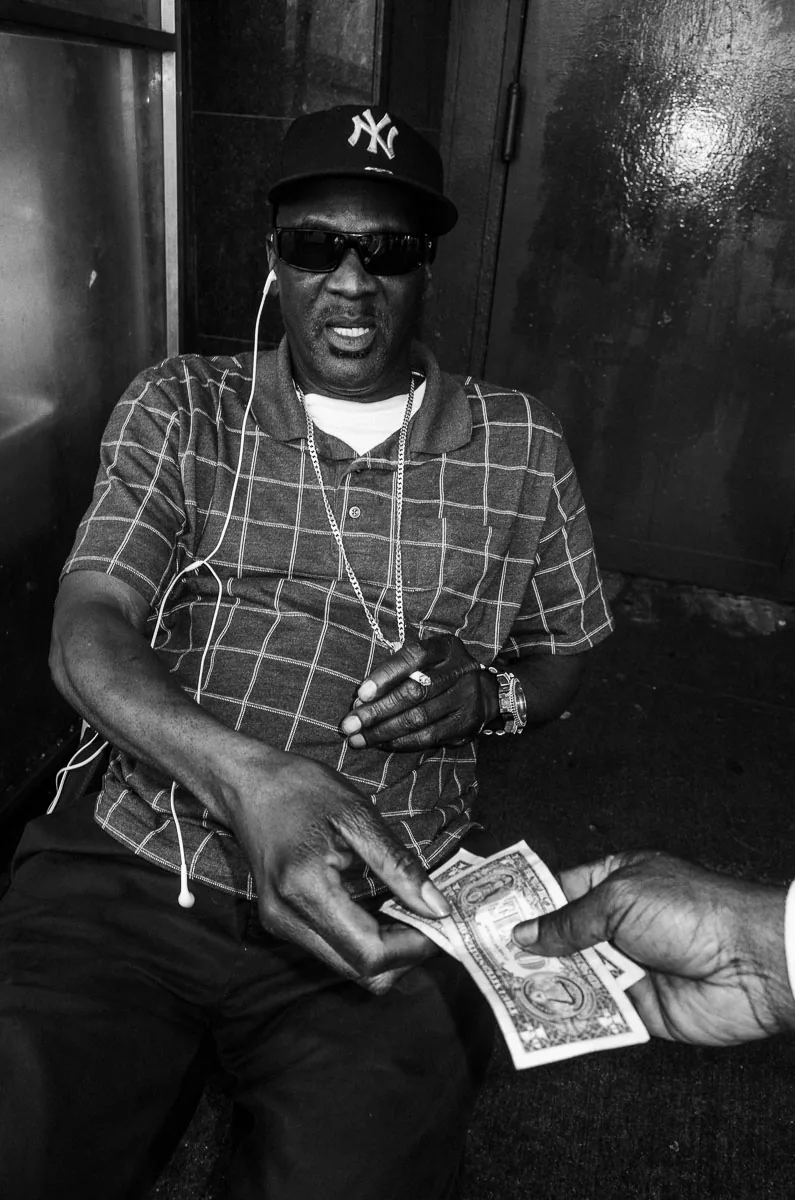 Old-school New York street portrait of a man in a Yankees cap receiving a dollar
