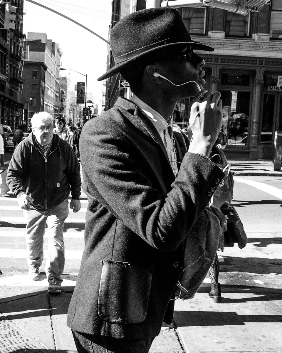 Black-and-white NYC street photograph of a man in a wide-brimmed hat at a crosswalk