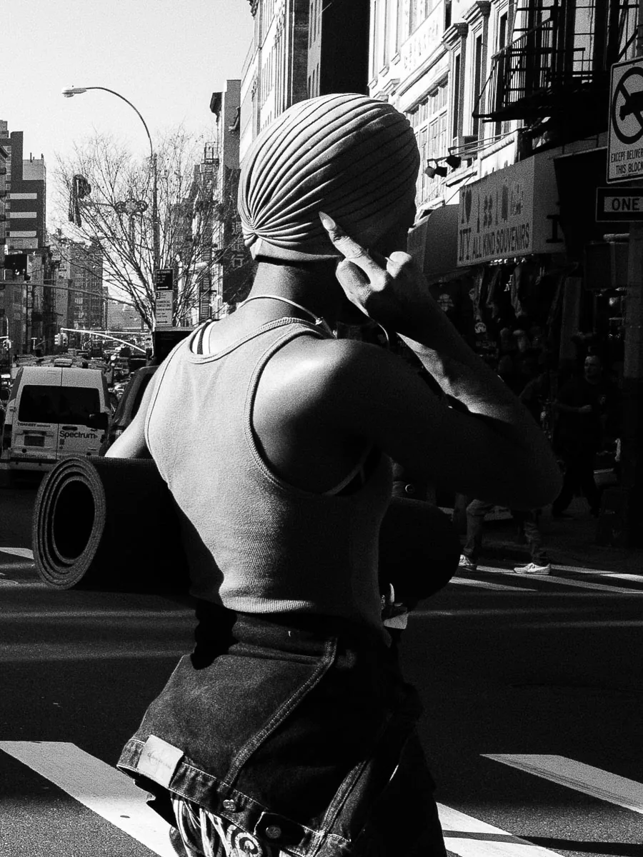 New York City black-and-white street photograph of a woman in a head wrap crossing the street