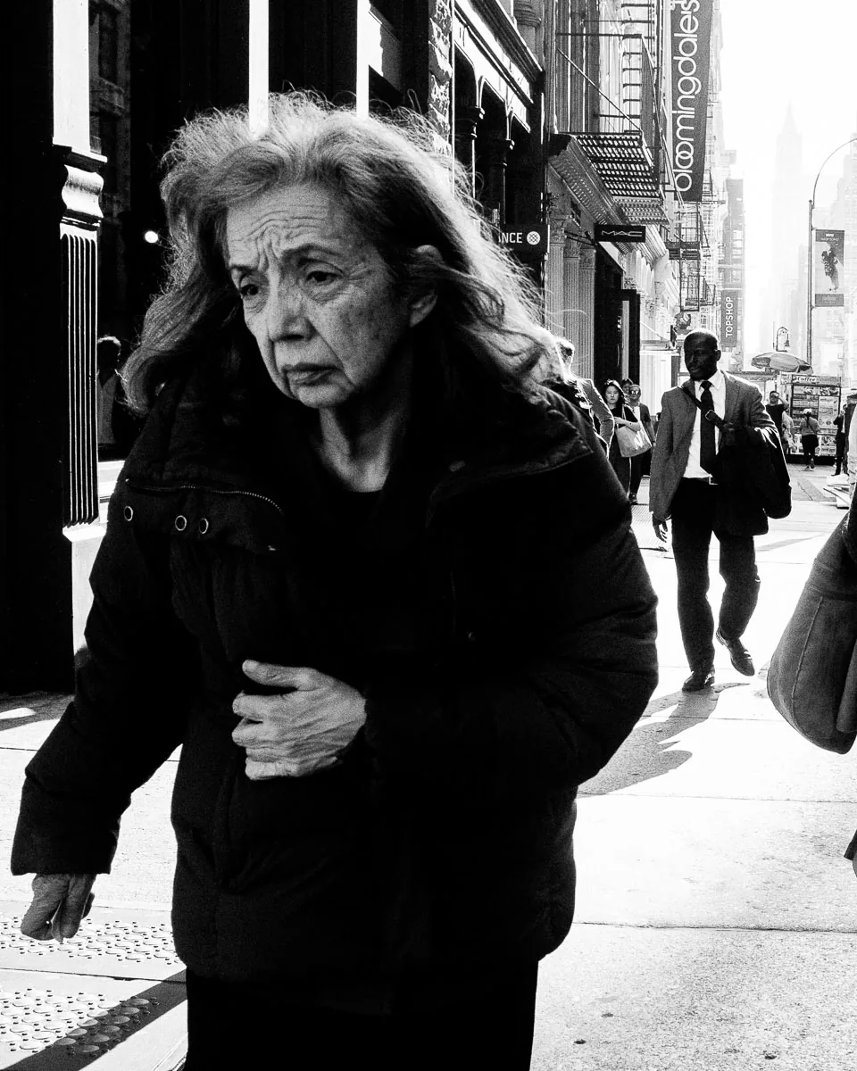 Emotional black-and-white NYC street photograph of a woman walking along Broadway