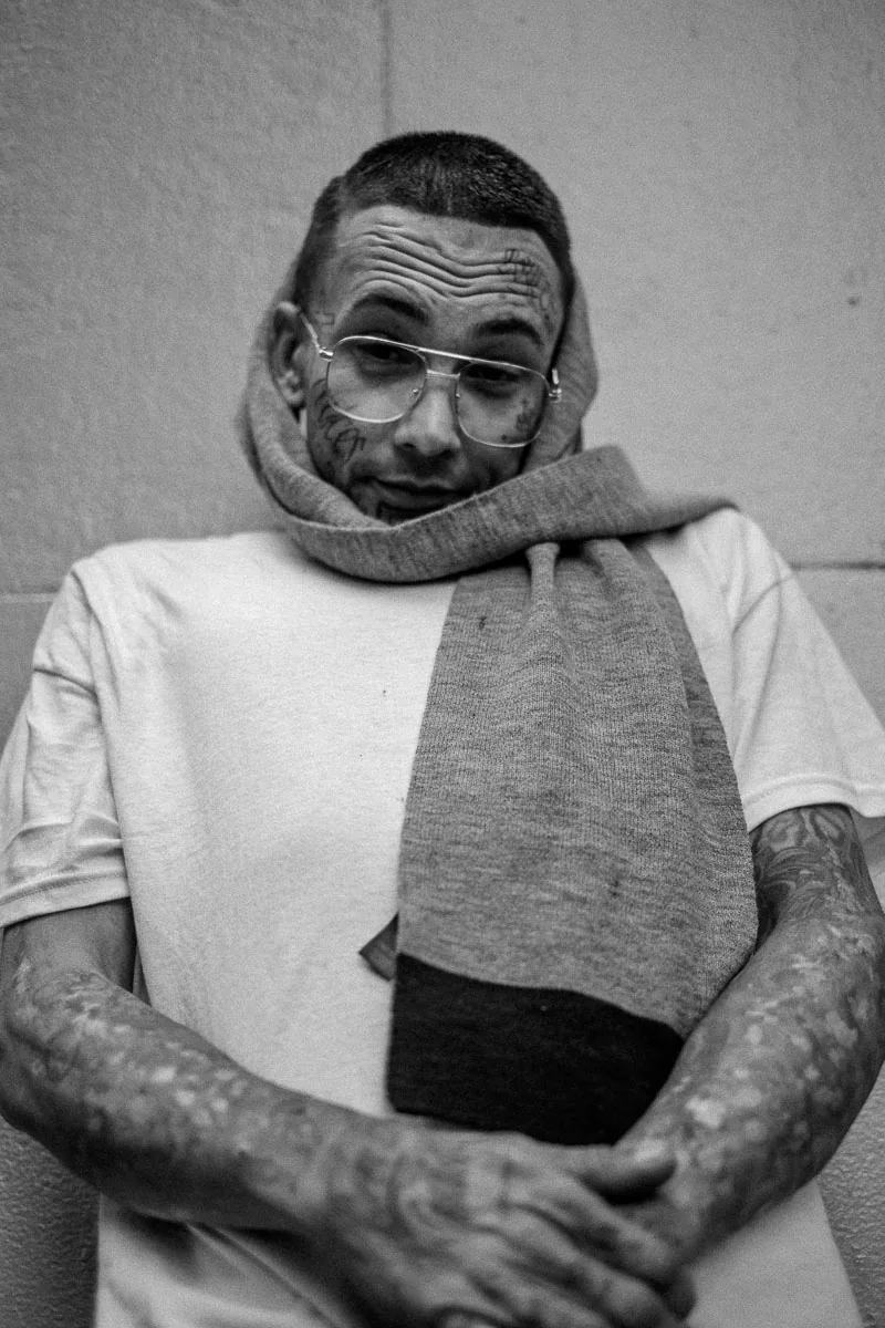 Black-and-white street portrait in NYC of a tattooed man wearing glasses and a scarf