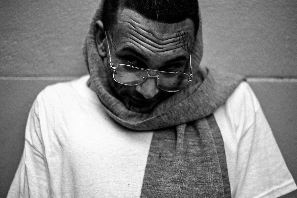 Black-and-white NYC street portrait of a tattooed man looking over his glasses