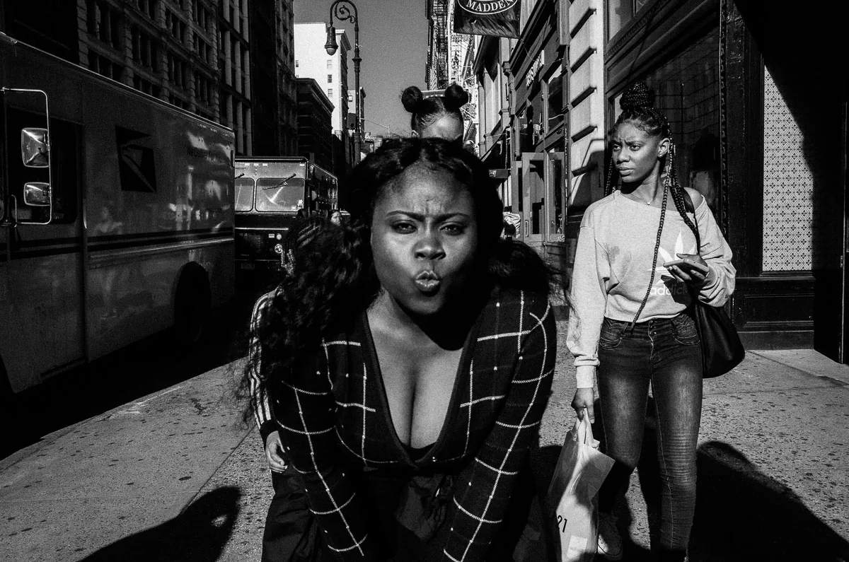Candid black-and-white NYC street photograph of three women on a crowded sidewalk