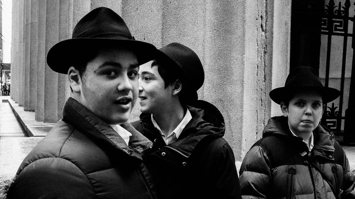 Black-and-white NYC street photograph of three boys in dark hats looking at the camera